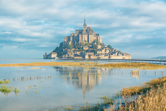 Mont Saint-Michel reflected across flooded marshland and shallow water after high tide in Normandy, France. Gothic monastery in Normandie. French architecture, cultural travel, coastal scenery