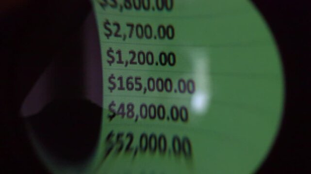 Close-up magnifying glass view of green financial numbers on a digital screen