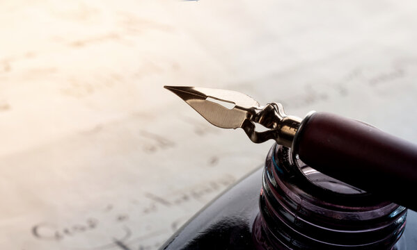 Fountain pen on an antique inkwell. Vintage nib pen and handwritten. Old history background. Retro style.