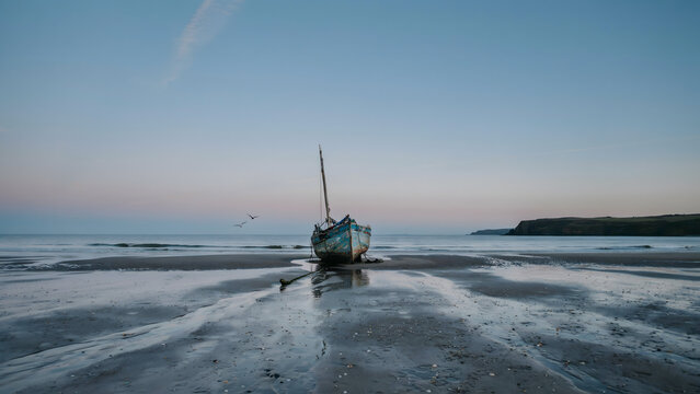 An old fishing boat rests on the wet sand at low tide isolated on a transparent background