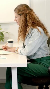 Vertical video: Starting work notes, woman in denim reflecting, resuming writing in office with cup