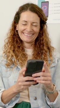 Vertical video: Smiling at message, woman in denim jacket scrolling smartphone in nook, poster