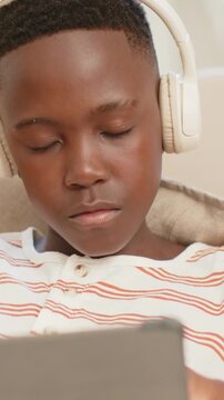 Vertical video: Tapping right hand on tablet, teen settling on couch at home, wearing white headset