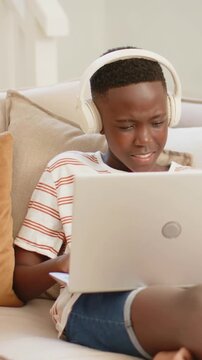 Vertical video: Watching laptop clip youth with headset, striped tee shifting into laughter at home