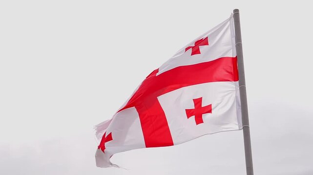 Georgian national flag with its five red crosses waving in slow motion on a flagpole against an overcast sky, representing a symbol of the country's patriotism and freedom slow motion