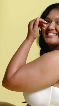 Vertical video: On photographer cue, model tucking hair, laughing in studio, revealing white top
