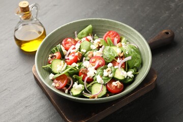 Fototapeta premium Appetizing spinach salad with cheese, walnuts and vegetables served on black textured table, closeup