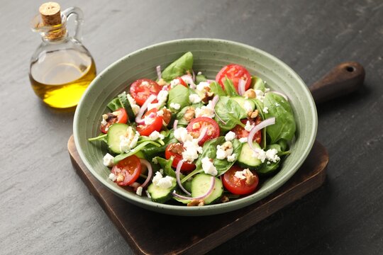 Appetizing spinach salad with cheese, walnuts and vegetables served on black textured table, closeup