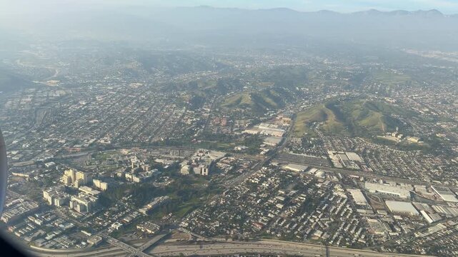 Aerial view of Los Angeles during landing, seen through an airplane window. Expansive cityscape, urban grid and clear skies capture the excitement of arriving in Southern California.