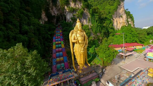 Cinematic FPV drone flight around the iconic Lord Murugan statue and colorful stairs at Batu Caves in Kuala Lumpur, Malaysia. Famous Hindu landmark surrounded by dramatic limestone cliffs.