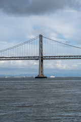 Obraz premium Bridge pier of the San Francisco–Oakland Bay Bridge beneath a softly clouded sky with subtle blue tones. A striking architectural landmark on the San Francisco waterfront.