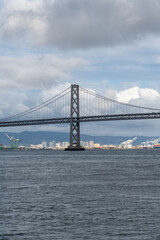 Obraz premium Bridge pier of the San Francisco–Oakland Bay Bridge beneath a softly clouded sky with subtle blue tones. A striking architectural landmark on the San Francisco waterfront.
