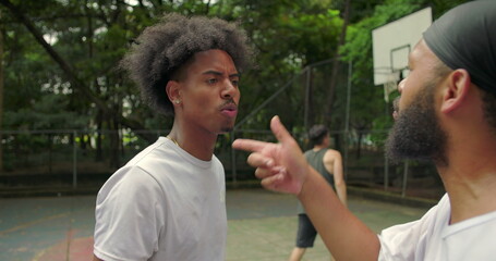 Fototapeta premium Two African American men arguing on outdoor basketball court, one pointing finger and pushing the other away during heated confrontation and emotional conflict