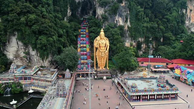 Aerial view of iconic Lord Murugan statue and colorful stairs at Batu Caves in Kuala Lumpur, Malaysia. Famous Hindu landmark surrounded by dramatic limestone cliffs.