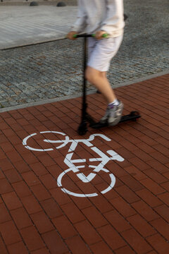 Person riding scooter over bicycle lane marking on brick pavement