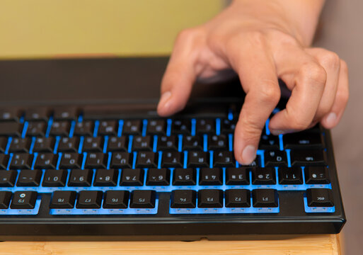 Gamer hand typing on rgb backlit mechanical keyboard close up