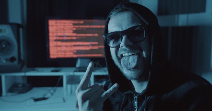 Hooded man smiling and making a victory hand gesture in front of computer code, representing successful hacking, cybercrime, and digital security concepts.