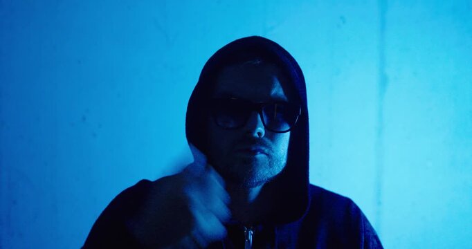 Hooded man wearing sunglasses in dramatic blue lighting, representing cybercrime, anonymity, hacking, and digital security concepts.