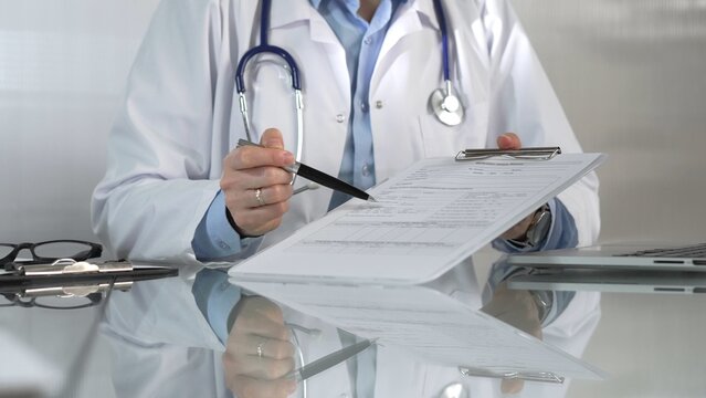 Female doctor, wearing a blue blouse under a medical coat, is pointing at medical chart, showcasing expertise in a close up shot. Medicine concept