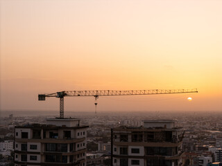 City skyline during golden hour with a building construction site and crane silhouetted against the sun © hcarbuccia