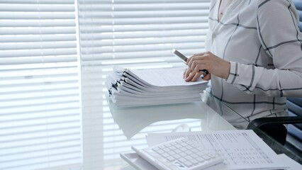 Professional is meticulously examining financial documents with a magnifying glass while writing...