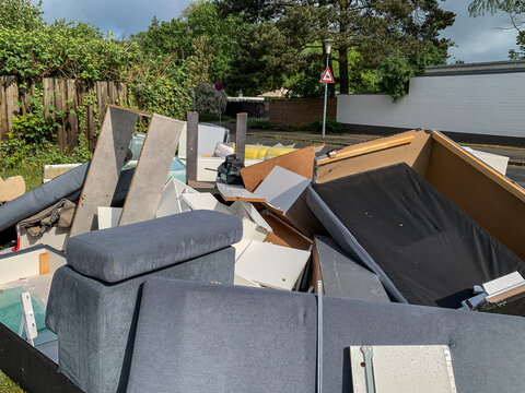 A large pile of discarded old furniture, including sofas, mattresses, and wooden cabinets, left on a sidewalk for bulky waste collection in Germany