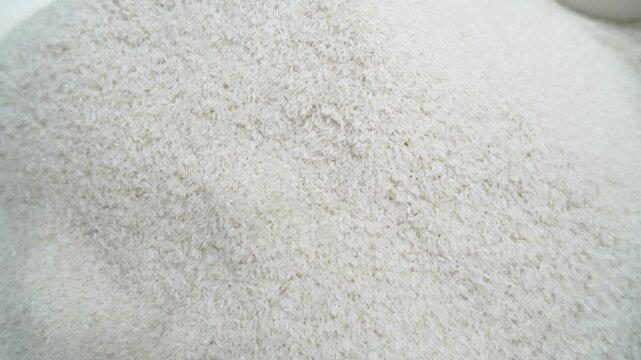 White rice grains are poured into the tray with slow movements.