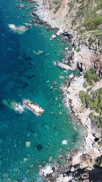 Ascending vertical aerial shot of crystal clear turquoise sea and rocky Mediterranean coastline.