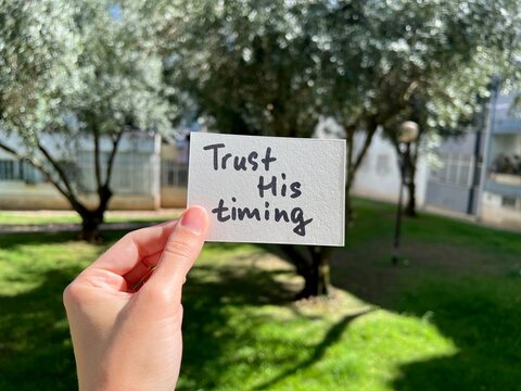 Trust His timing - hand with christian text outdoors, biblical faith and trust Lord concept	