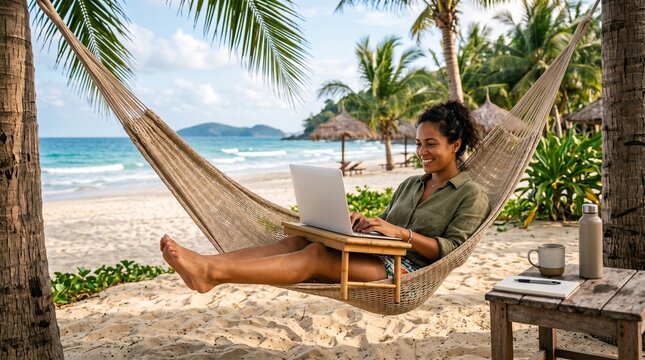 Woman working on laptop in hammock on tropical beach paradise with ocean view and palm trees