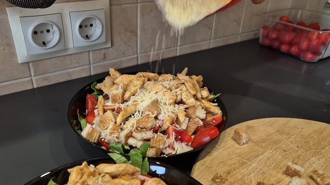 Close up view of pouring a generous amount of finely grated parmesan cheese onto a fresh caesar salad