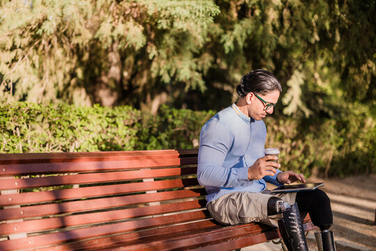 Disabled latino man resting with coffee and tablet in park