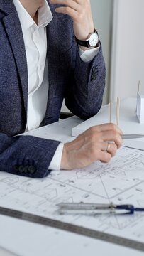 Professional architect analyzing blueprint plans, developing new design concepts for a construction project, holding a tool at a desk with an architectural model
