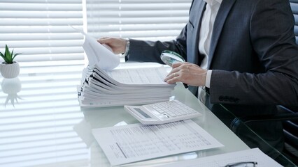 Fototapeta na wymiar Professional businessman using a magnifying glass to meticulously examine financial reports and paper documents on a desk, analyzing data for audit or investigation purposes