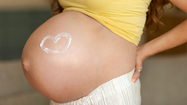 Closeup of pregnant belly with heart shape drawn in moisturizer cream