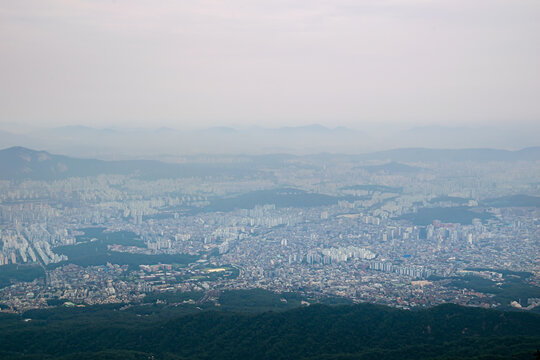 Panoramic Seoul skyline surrounded by mountains and forested hills under hazy atmosphere
