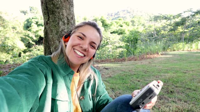 Happy woman listening music with vintage headphones at park city - Girl doing selfie sitting on grass - Nostalgia lifestyle trend
