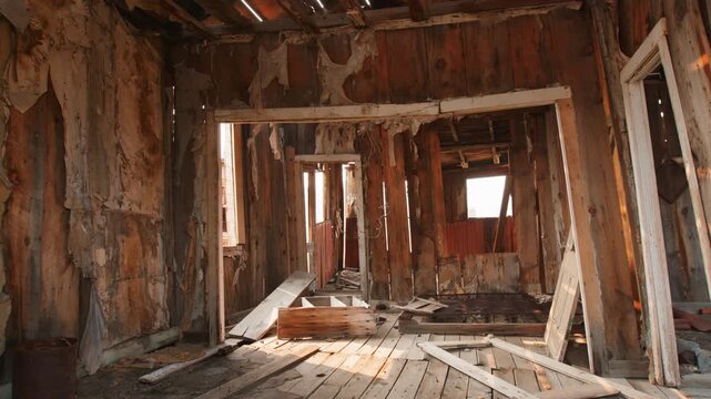 Interior view of dilapidated wooden building in abandoned ghost town, featuring peeling wallpaper, exposed timber framing, scattered debris on warped floorboards.