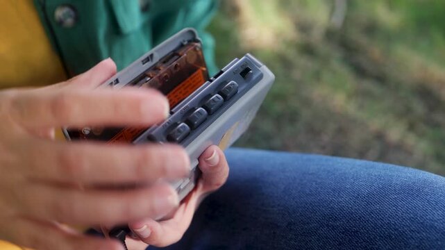 Person inserting cassette tape into portable player outdoors - Retro audio and nostalgia lifestyle trend