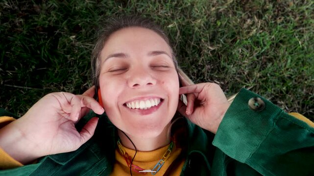 Happy woman listening music with vintage headphones at park city - Girl dancing while lying on grass - Nostalgia lifestyle trend