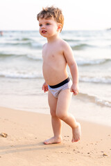 Young child standing on sandy beach, looking down at gentle waves along calm shoreline © Mikhail Mishchenko