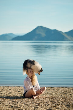 A woman hugs her Shetland Sheepdog while sitting beside a peaceful mountain lake. Beautiful lifestyle portrait expressing love, companionship, and emotional connection.