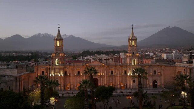 Aerial drone view of the Basilica Cathedral of Arequipa illuminated at dusk with the iconic Misti volcano in the background. Historic city center and famous landmark in southern Peru.