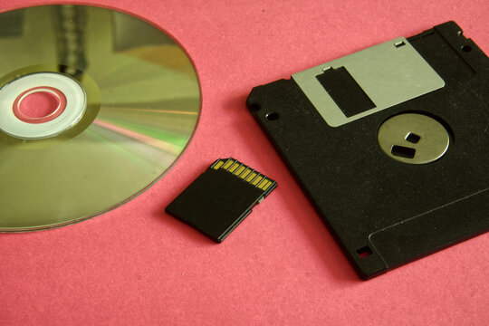 Representing the evolution of digital storage with cd-rom, sd card, and floppy disk against a pink background