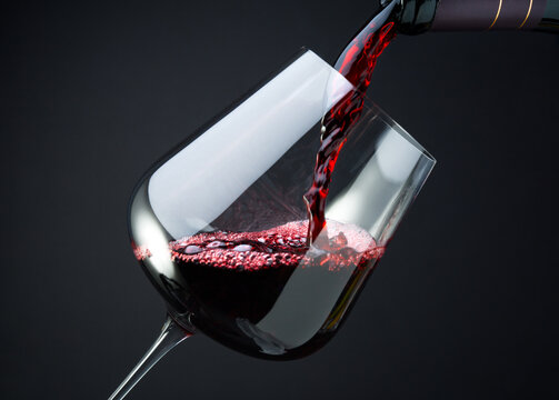 Red wine is pouring into a glass from a bottle, close up 