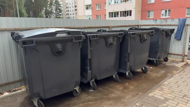 Row of large grey wheeled garbage bins lined up near a metal fence in a residential area. Waste management, urban, outdoors, recycling