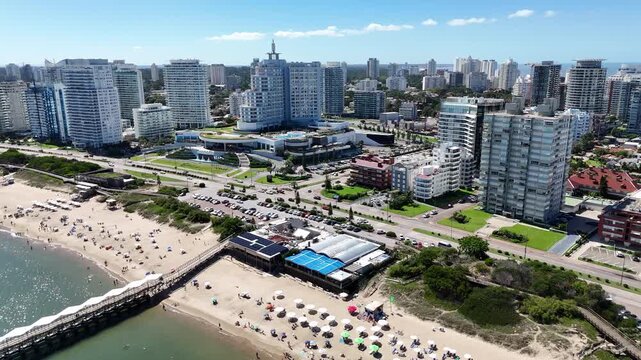 Drone view of Mansa Beach, the iconic wooden pier, turquoise waters and the modern skyline of Punta del Este on a sunny summer day in Uruguay.	
