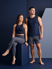 Fototapeta premium Athletic Caucasian Couple in Matching Navy Charcoal Beachwear Posing on Studio Block, Premium Resort Wear Fitness Editorial Portrait