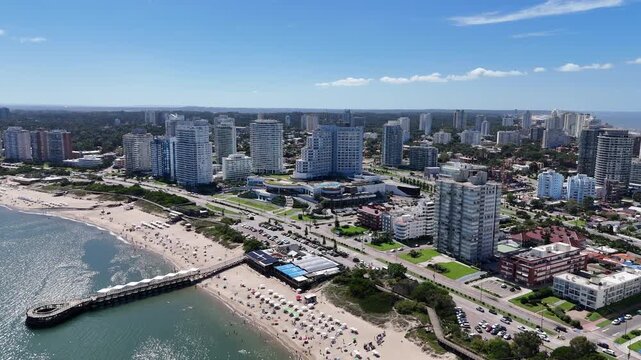 Drone view of Mansa Beach, the iconic wooden pier, turquoise waters and the modern skyline of Punta del Este on a sunny summer day in Uruguay.