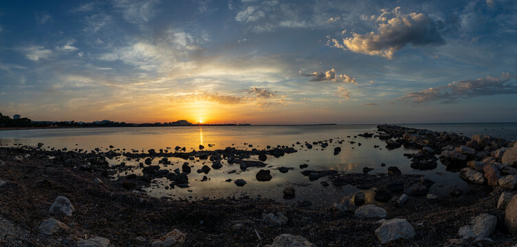 Sun sets over the Mediterranean Sea at Costa Blanca with dark rocks in the foreground and clouds in the evening sky